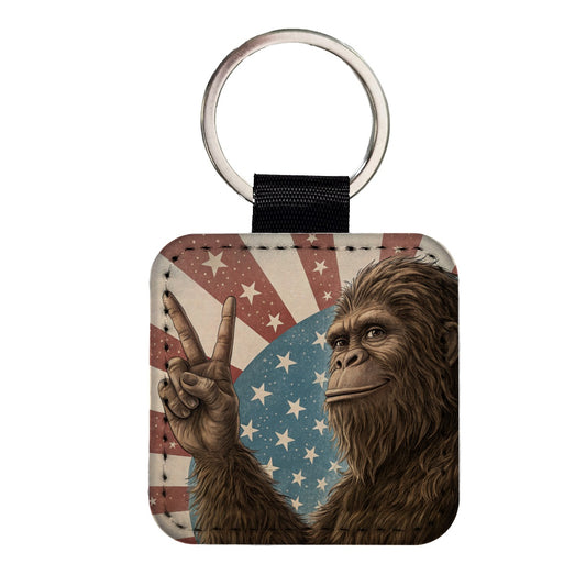 Bigfoot Giving Peace Sign Rising American Flag Square Faux Leather Keychain